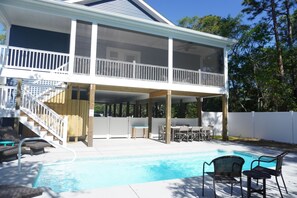 Ein zweistöckiges Haus mit überdachter Terrasse, Schwimmbad und Gartenmöbeln.