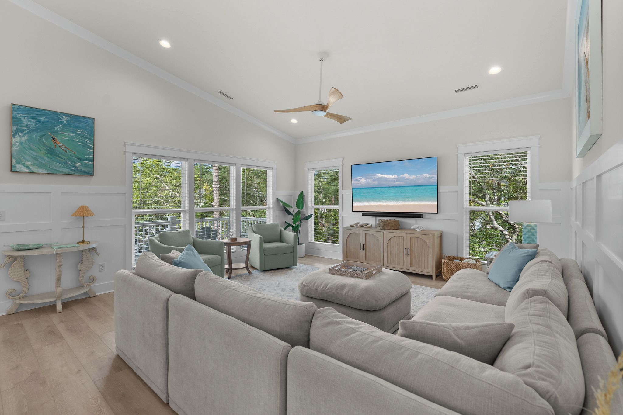 A spacious living room with a large sectional sofa, a television mounted on the wall, and a ceiling fan.