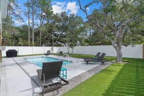 A backyard with a swimming pool, lounge chairs, and a covered grill area. - Saltwater Pool/Putting Green + Minutes to Beach (Oak Island)