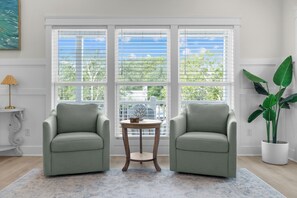 A room with two armchairs, a small round table, a potted plant, and a painting on the wall. - Saltwater Pool/Putting Green + Minutes to Beach (Oak Island)
