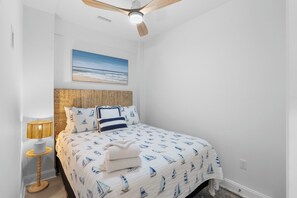 A bedroom with a bed, a ceiling fan, a wall-mounted picture, and a bedside lamp. - Saltwater Pool/Putting Green + Minutes to Beach (Oak Island)