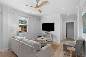 A modern living room with a sofa, armchair, TV, and ceiling fan. - Saltwater Pool/Putting Green + Minutes to Beach (Oak Island)