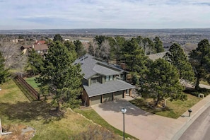 A residential house with a garage, surrounded by trees and a clear view of a distant cityscape.