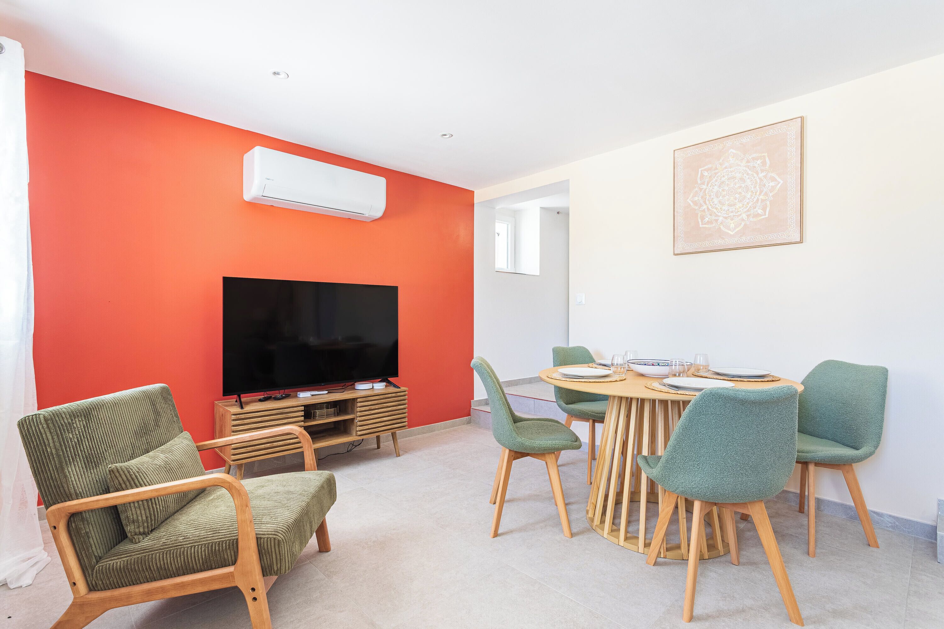 A modern living room with a flat-screen TV, a dining table with chairs, and a red accent wall.