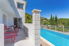 Ein Poolbereich mit freiem Blick auf den Pool, ein weißes Gebäude und eine Hügelkulisse im Hintergrund.