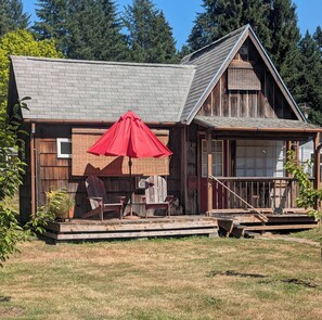 A rustic cabin with a porch, a red umbrella, and a wooden deck. - Adorable 1-bedroom detached Guest house, w/loft, AC, and beautiful deck, (Brush Prairie)