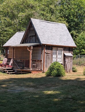 A rustic wooden cabin with a porch, a small garden, and a fence. - Adorable 1-bedroom detached Guest house, w/loft, AC, and beautiful deck, (Brush Prairie)