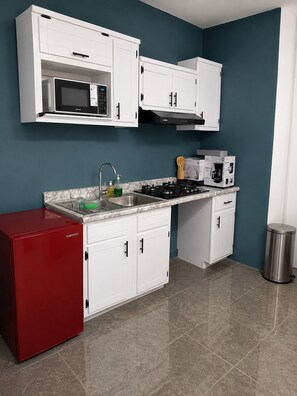 A compact kitchen with white cabinets, a red refrigerator, a microwave, a stove, and a coffee maker.