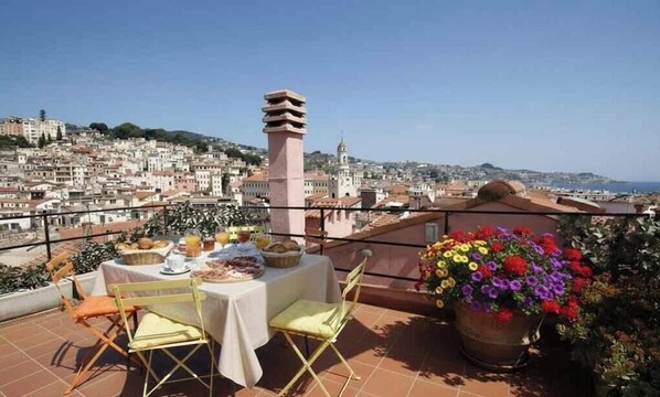 Eine Terrasse mit Frühstückstisch, mit Blick auf eine Stadtlandschaft mit Gebäuden und einem Turm.