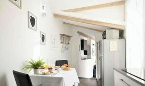 Ein Essbereich mit einem für das Frühstück gedeckten Tisch, einem Kühlschrank und einer sichtbaren Küche im Hintergrund.