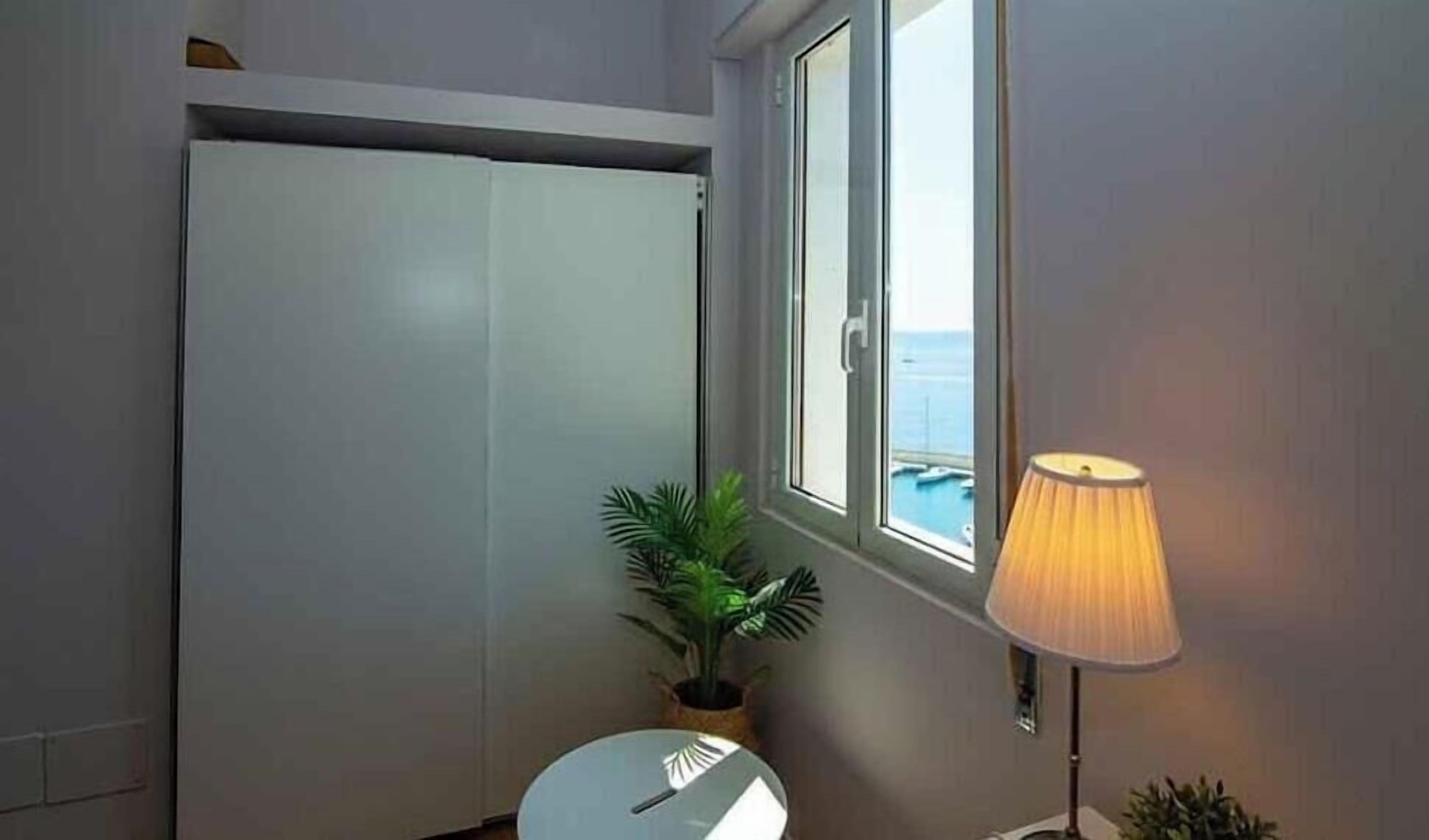 A bathroom with a toilet, a potted plant, a window with a view of the sea, and a lamp.