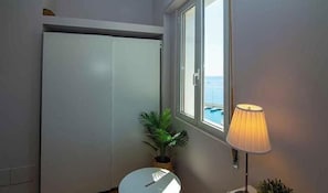 Ein Badezimmer mit Toilette, einer Zimmerpflanze, einem Fenster mit Meerblick und einer Lampe.