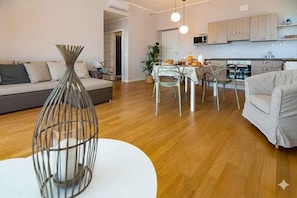 Ein modernes Wohnzimmer mit Sofa, Esstisch und Stühlen, einer Küchenzeile mit Schränken und einer weißen Vase auf einem Tisch.