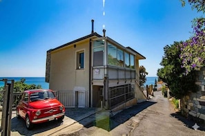 Ein zweistöckiges Haus mit Balkon, ein Auto davor und freier Meerblick.