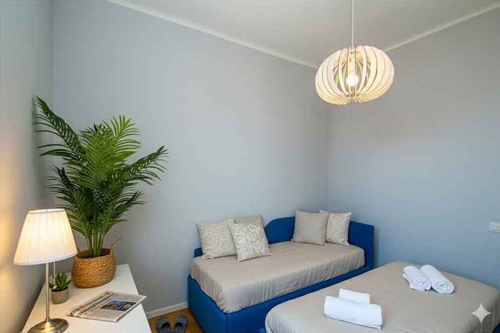 Une pièce comprenant un lit, une table de chevet avec une lampe, une plante en pot et un luminaire suspendu.