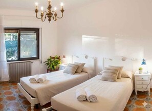 Ein Hotelzimmer mit zwei Betten, einer Kandelaber, einem Fenster und einer Pflanze.