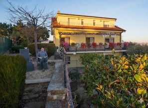Ein zweistöckiges Gebäude mit Balkon, umgeben von Grünflächen und einem Garten.