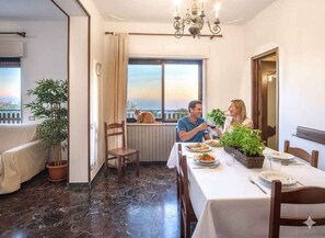 Ein Essbereich mit einem Tisch für zwei Personen, einer Topfpflanze und Blick auf den Himmel durch ein Fenster.