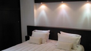 A bed with white bedding and pillows, a dark headboard, and wall-mounted lights. - Hotel Mar Azul by Croma (Santa Marta)