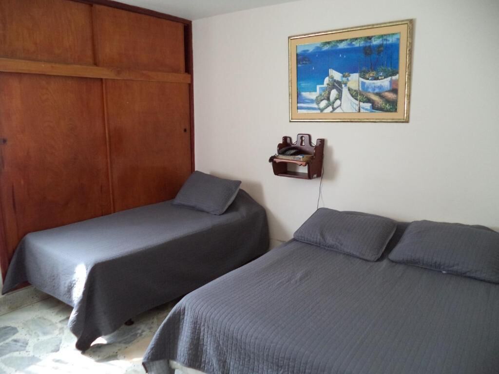 Una habitación con dos camas, un armario de madera, un cuadro en la pared y un pequeño estante con objetos.