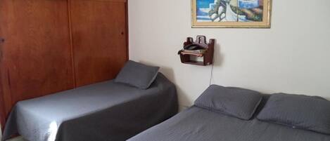 Una habitación con dos camas, un armario de madera, un cuadro en la pared y un pequeño estante con objetos.