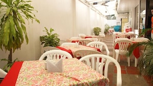 A restaurant with white chairs and tables, some with red tablecloths, and potted plants. - Hotel Mar Azul by Croma (Santa Marta)