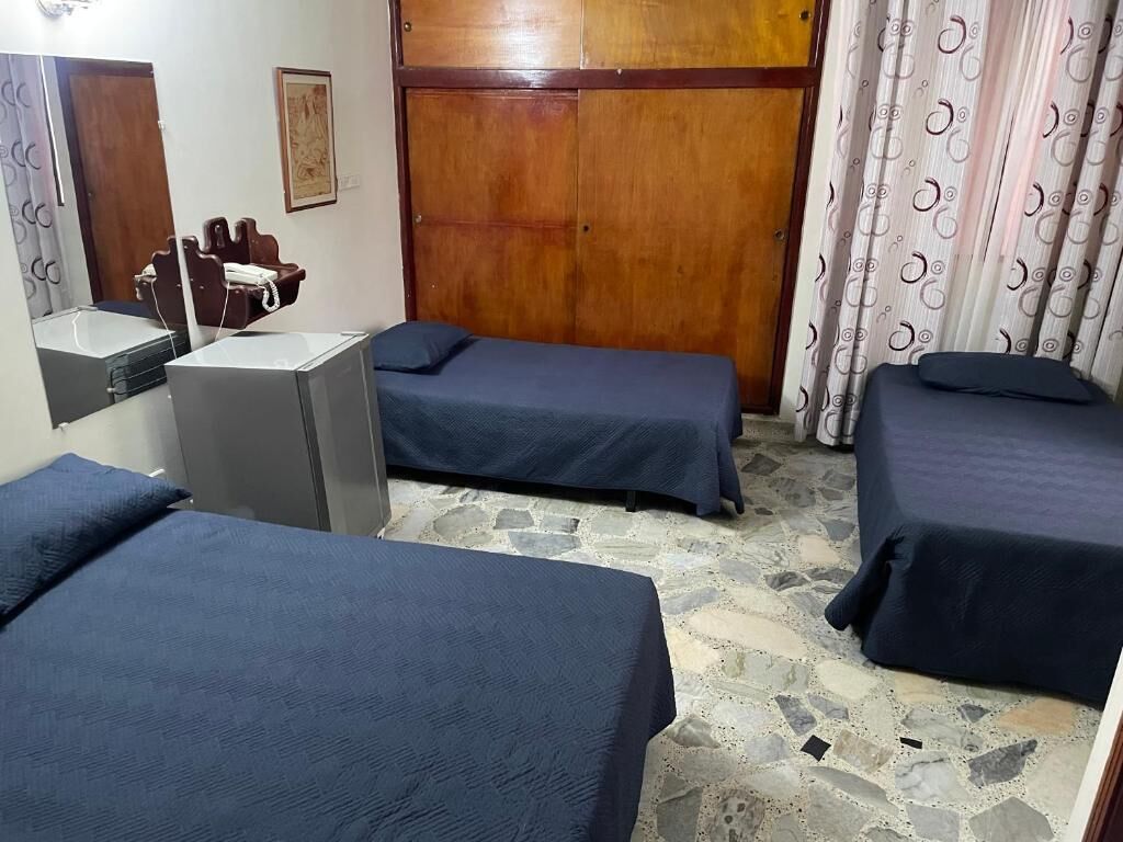 Quarto com duas camas, um guarda-roupa de madeira, uma pequena mesa com uma cadeira e um espelho.