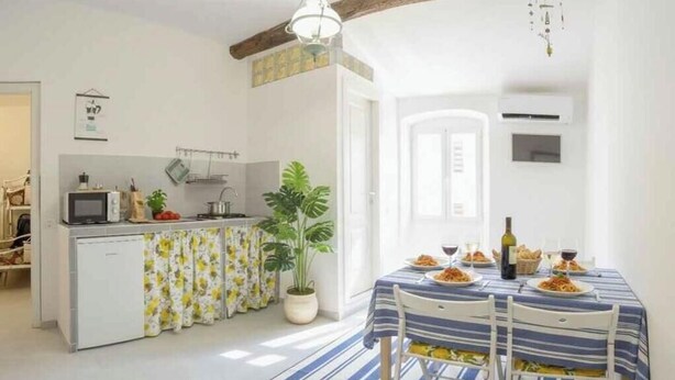 Eine kleine Küche mit Mikrowelle, Spüle und einem Blumentopf. Ein Esstisch mit Stühlen ist für eine Mahlzeit gedeckt.
