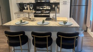 Une cuisine moderne dotée d’un îlot central, d’appareils électroménagers en acier inoxydable et de luminaires suspendus.