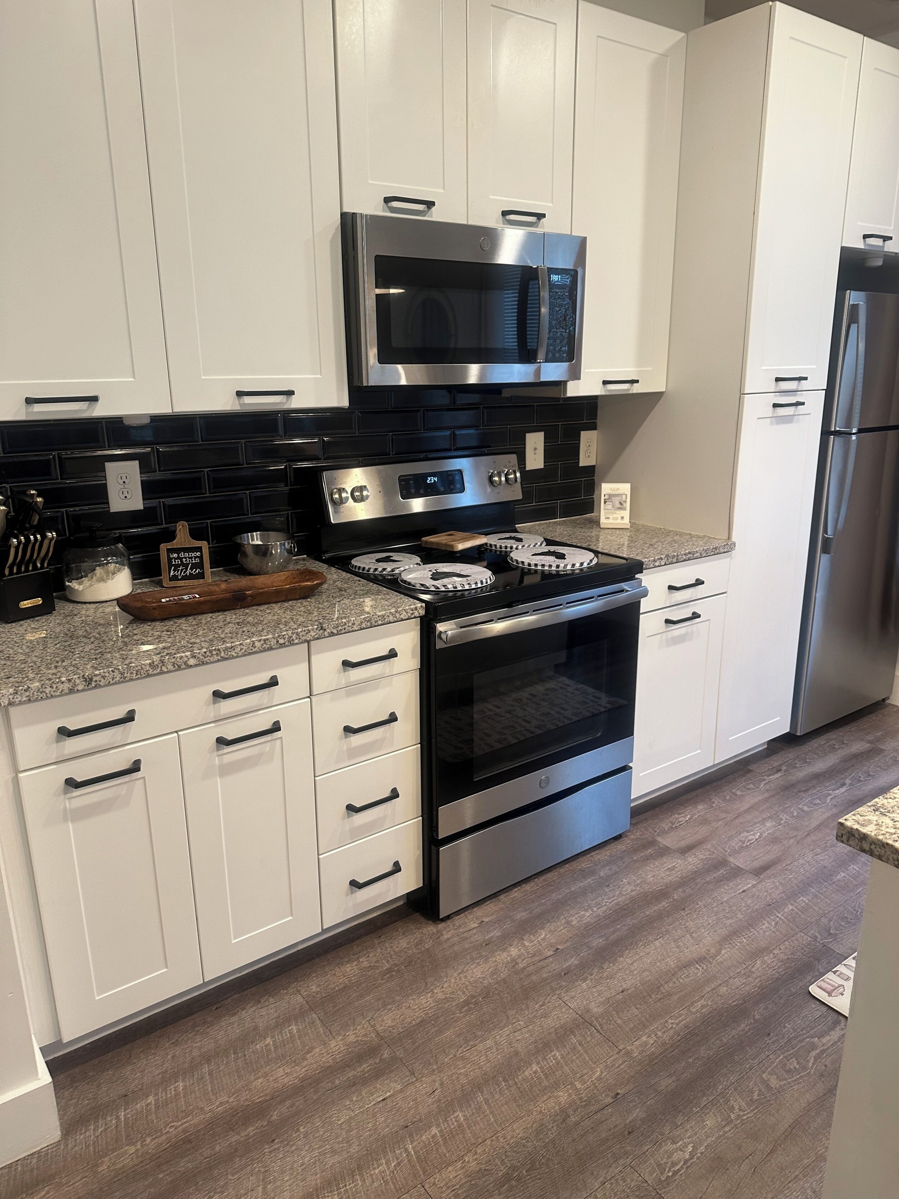 A kitchen with white cabinets, a stainless steel stove, a microwave, and a refrigerator.