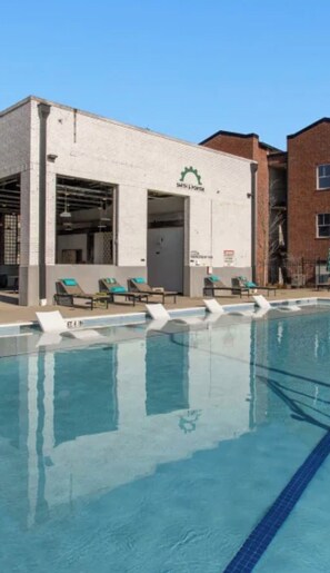 Ein Schwimmbecken mit Liegestühlen, ein Gebäude mit der Aufschrift 'SOUTH & PORTER' und ein strahlend blauer Himmel.