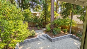 A backyard with a paved patio, a wooden fence, and various trees and shrubs. - Stylish 3BR Kirkland Haven with Backyard Grill (Kirkland)