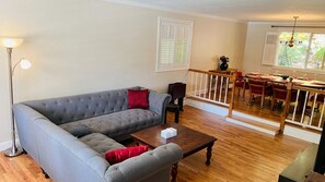 A living room with a grey sofa, a wooden coffee table, and a dining area with a wooden railing and table. - Stylish 3BR Kirkland Haven with Backyard Grill (Kirkland)