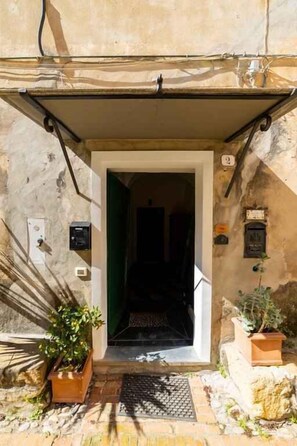 A doorway leading into a building with a tiled floor, a potted plant to the left, and a wall-mounted sign to the right. - Holiday apartment with air conditioning (Cervo)
