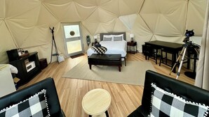 Una habitación tipo tienda de campaña con una cama, un escritorio, una silla, una mesa y un trípode.