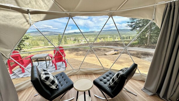 Una tienda de campaña con vistas a un paisaje montañoso, dos sofás de cuero negro, una mesa redonda pequeña y sillas rojas.
