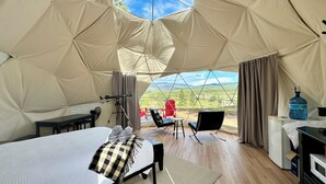 Alojamiento en tienda de campaña con cama, zona de estar y vistas al exterior.