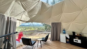 Una habitación con tienda de campaña que ofrece vistas a un paisaje montañoso, un telescopio, una silla, una mesita y un dispensador de agua.