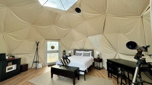 Una habitación con carpa, una cama, un escritorio, una silla, un trípode y una ventana.