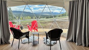 Une pièce aménagée sous une tente, avec deux fauteuils en osier, une petite table et une vue sur un paysage montagneux.