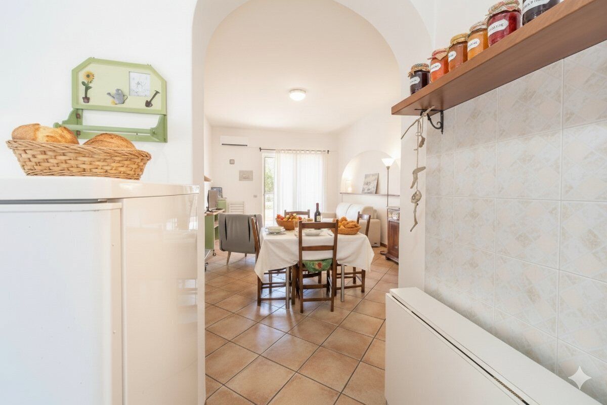 Une cuisine équipée d’une table à manger, de chaises, d’un réfrigérateur et d’une étagère où sont rangés des bocaux.