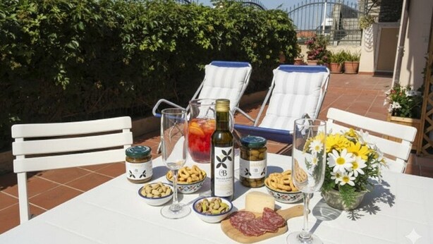 A table set with food, drinks, and a bottle of wine on a terrace with chairs and a hedge in the background. - Studio with air conditioning and terrace (Santo Stefano Al Mare)