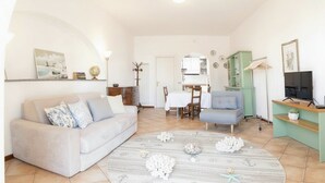 A living room with a sofa, a dining table, and a TV stand. - Studio with air conditioning and terrace (Santo Stefano Al Mare)
