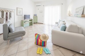 Ein Wohnzimmer mit einem grauen Sofa, einem weißen Sofa, einer farbenfrohen Streifen Tasche und einem Strohhut auf dem Boden.