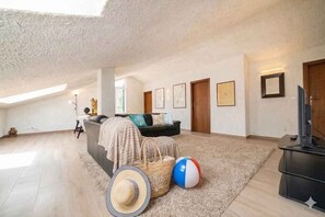 A spacious loft with a high ceiling, a cozy seating area with a sofa and cushions, a television, and a large window providing natural light. - Villa with garden and terrace (Imperia)