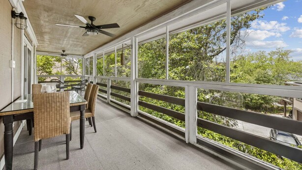 Un'area esterna coperta con tavolo e sedie, ampie finestre e una ventola a soffitto.