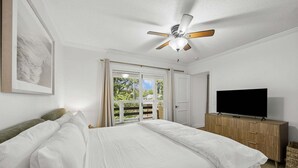 Una camera da letto con un letto, una televisione, un ventilatore a soffitto e una finestra vista verde.