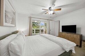 Ein Schlafzimmer mit Bett, Fernseher, Deckenventilator und Fenster mit Blick ins Grüne.