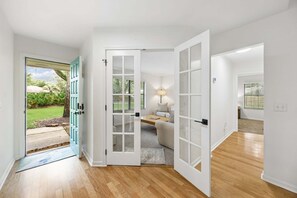 A hallway with a wooden floor, a white door, and a view of a garden outside. - Quiet Neighborhood, Fenced Yard, Dog Friendly (Fernandina Beach)
