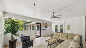 En overdækket terrasse med en ventilator, en sofa, et bord og en potteplante.